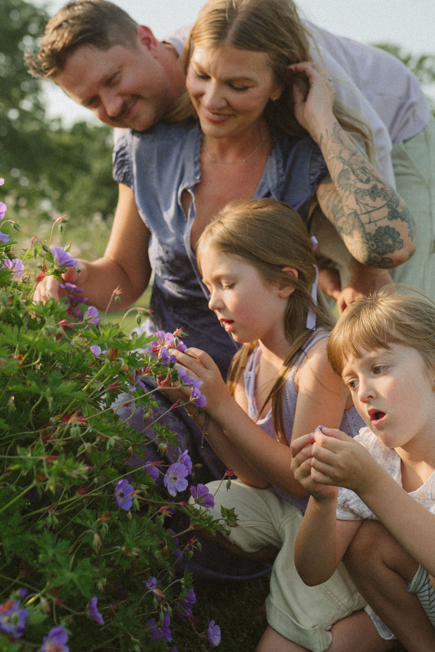 Group leaning in to smell and examine purple wildflowers growing in a garden.