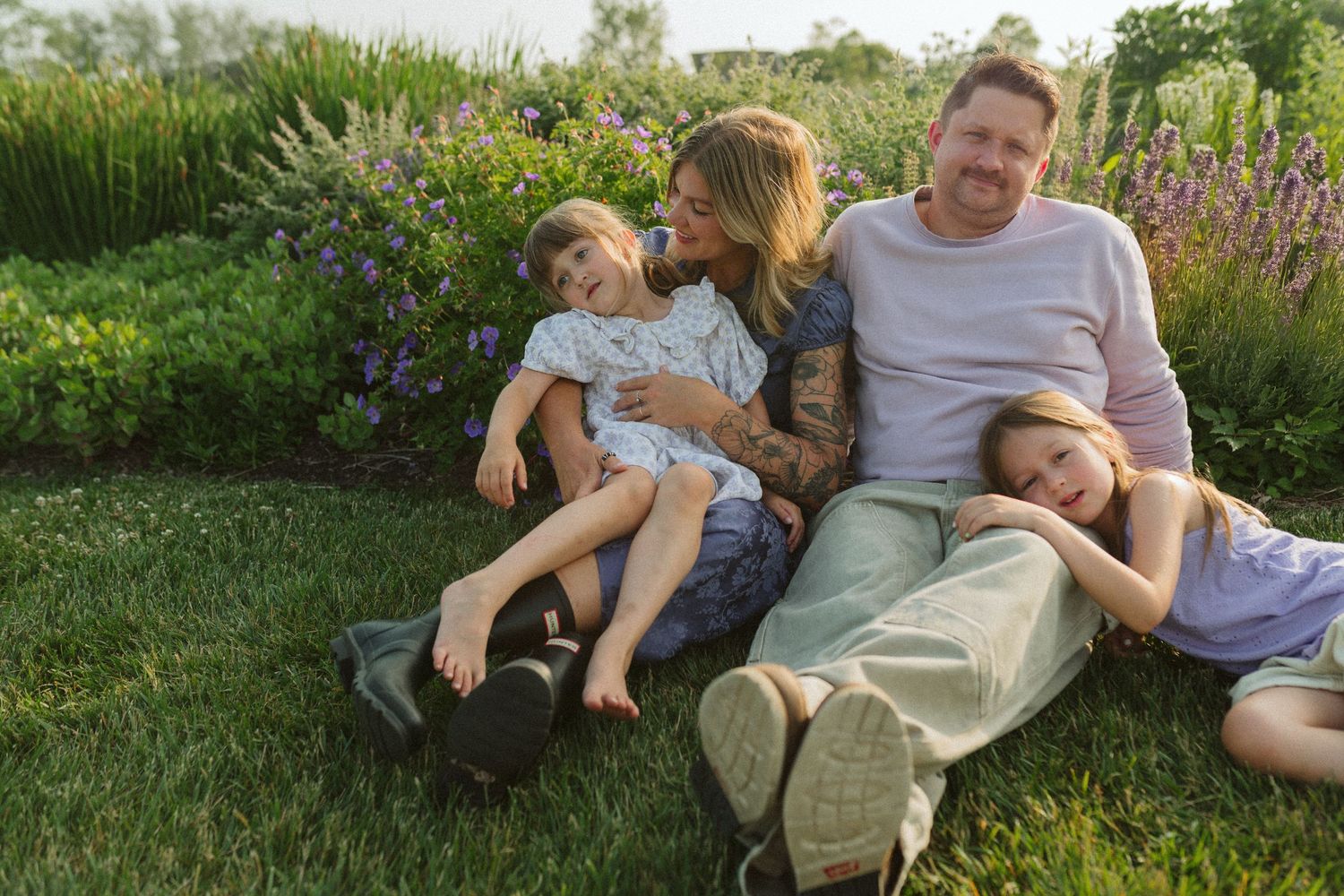 A family relaxes together on green grass in a garden setting during a sunny summer day.