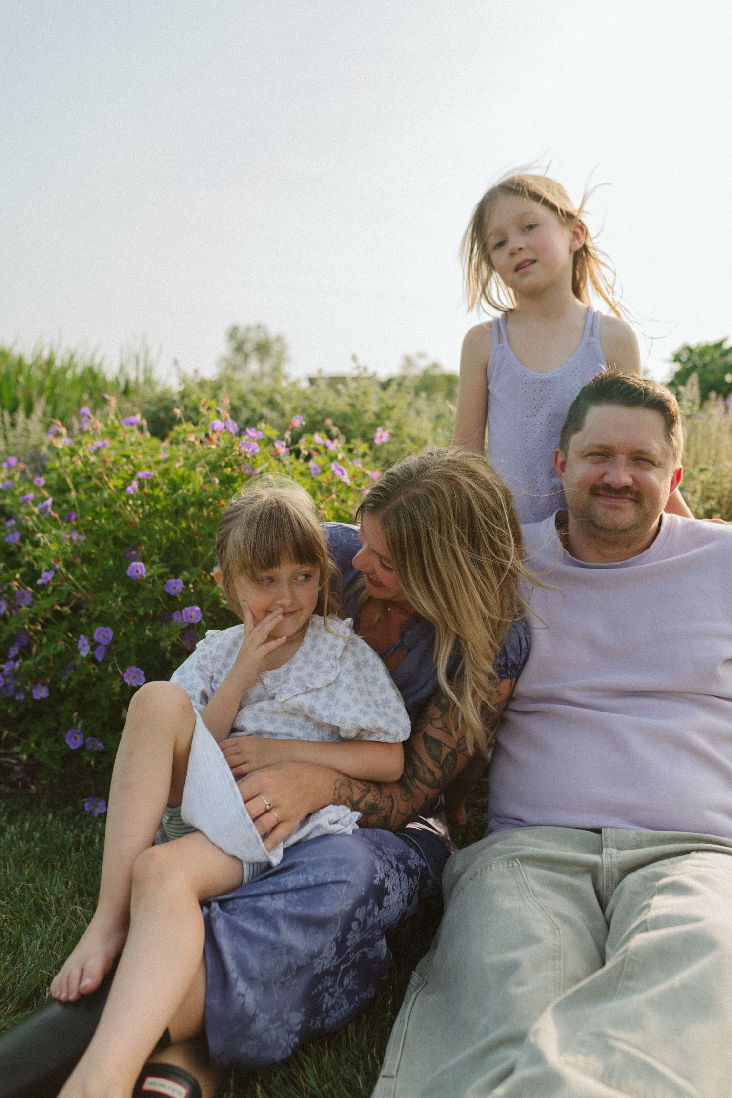 Family relaxing together on a sunny hillside surrounded by colorful summer flowers.