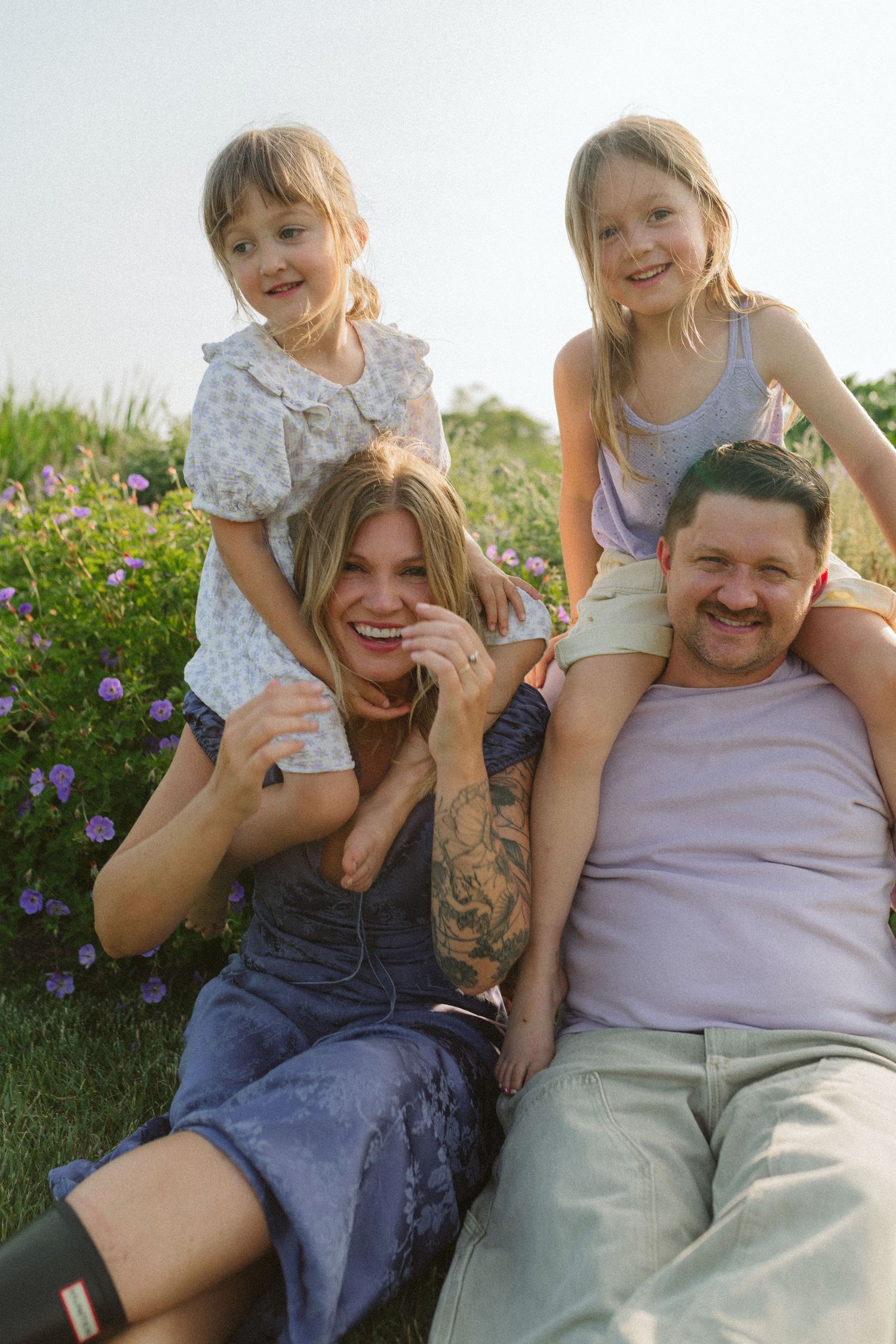 A playful family moment captured in a series of photos showing joyful interaction while laying in grass near purple flowers.