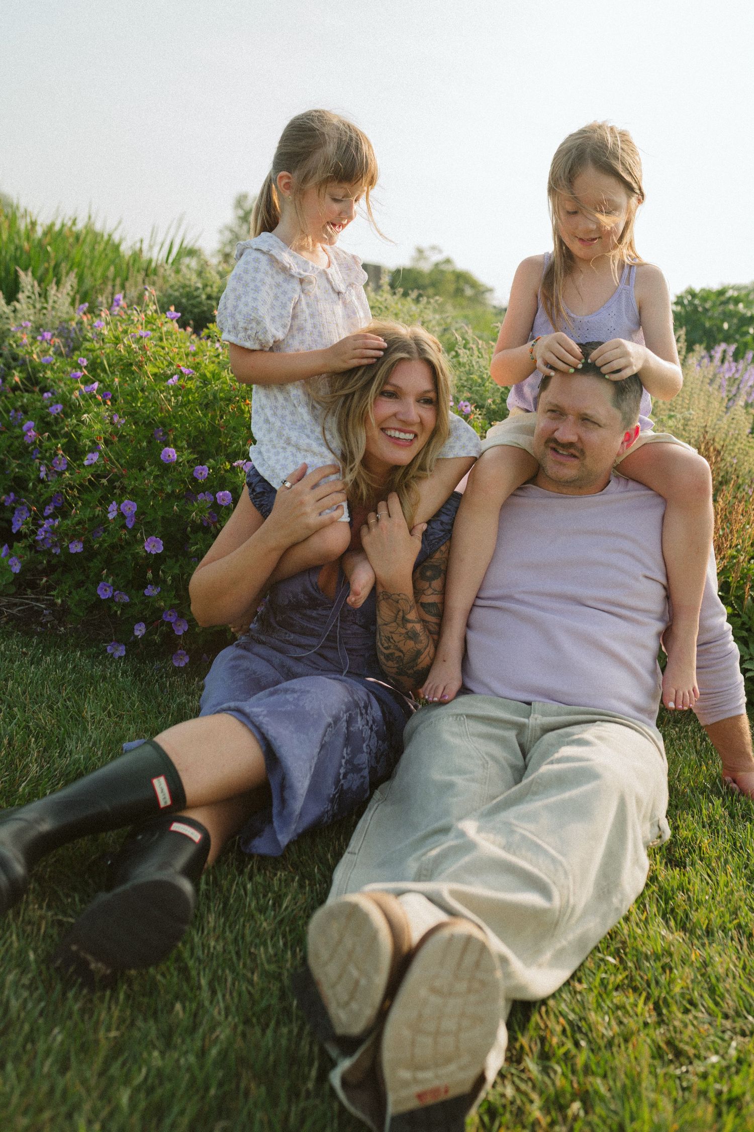 Family enjoying a tender moment together while relaxing on grass with flowers in the background.