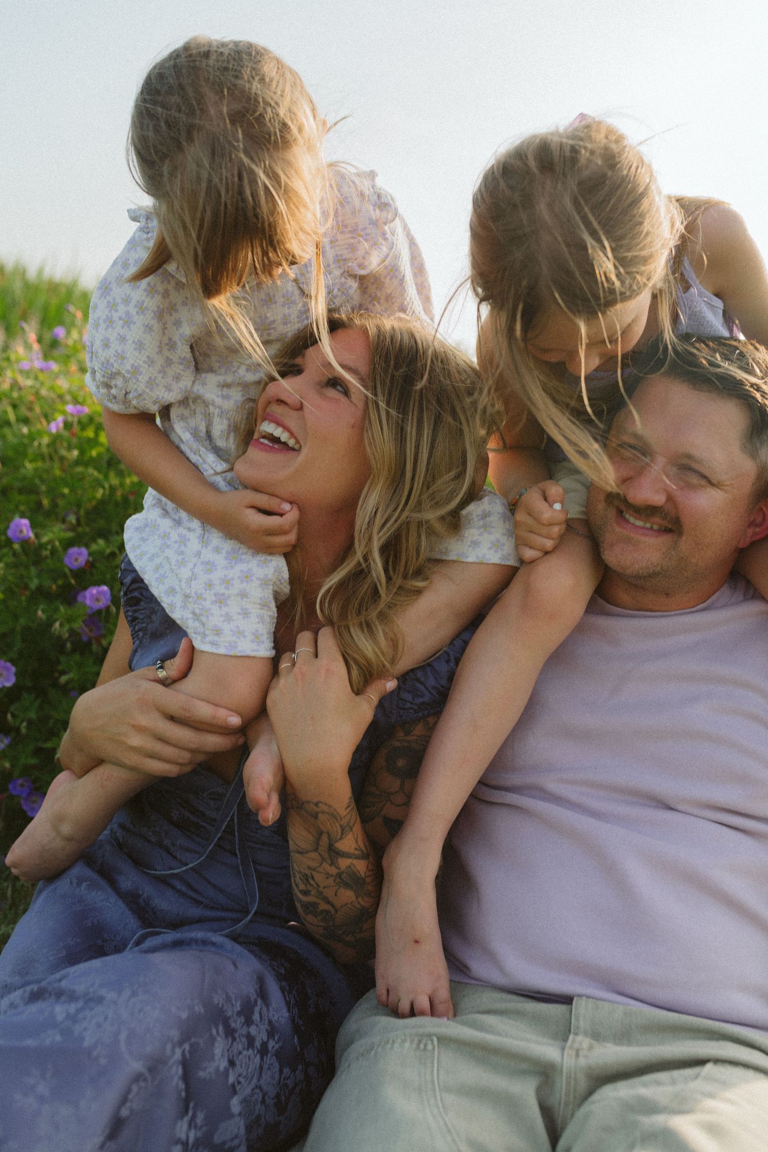 Candid moments of laughter and joy shared while laying together on grass near flowering plants.