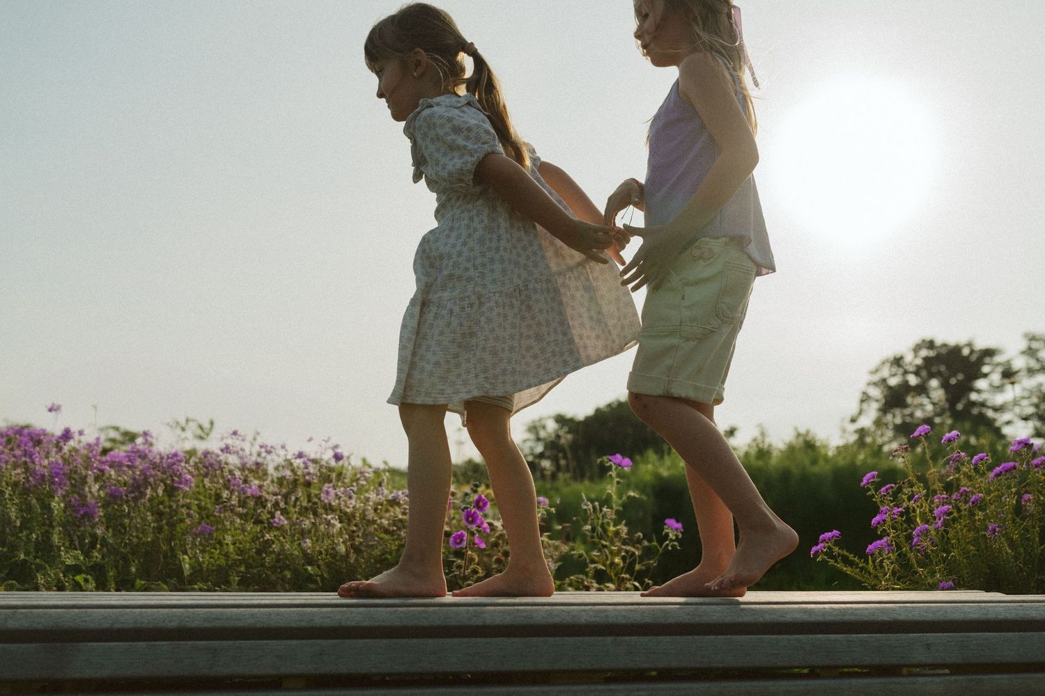 Kids playing and jumping on a wooden deck surrounded by wildflowers at sunset.