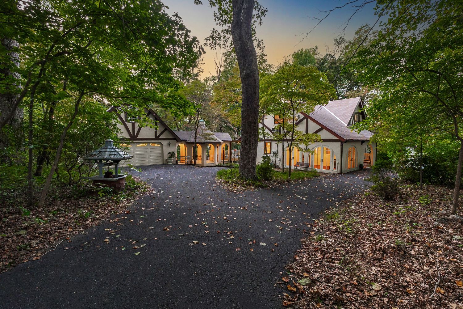 Wooded pathway with fall leaves leading through a serene residential area at dusk.