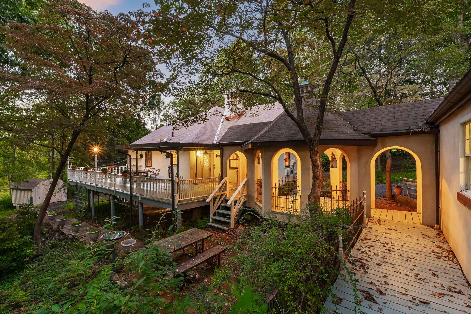 Charming cottage-style home with arched doorways illuminated at twilight among trees.