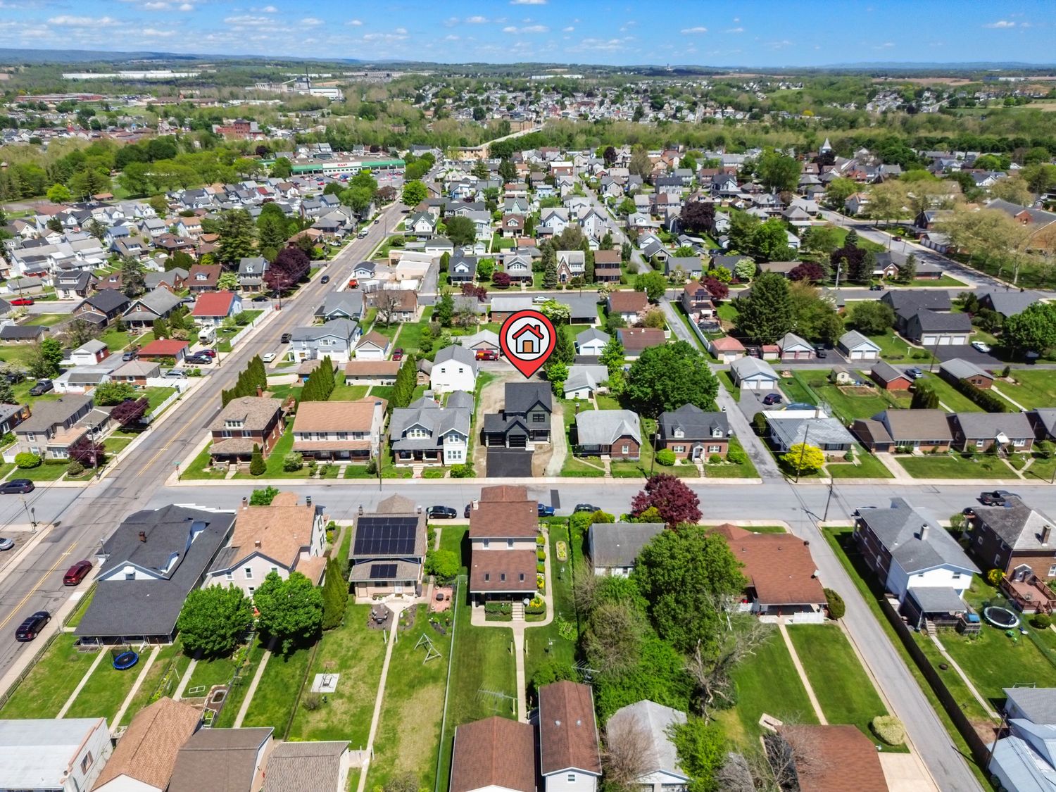 Aerial drone view of a suburban neighborhood with tree-lined streets, residential homes, and a highlighted property marked with a red pin.