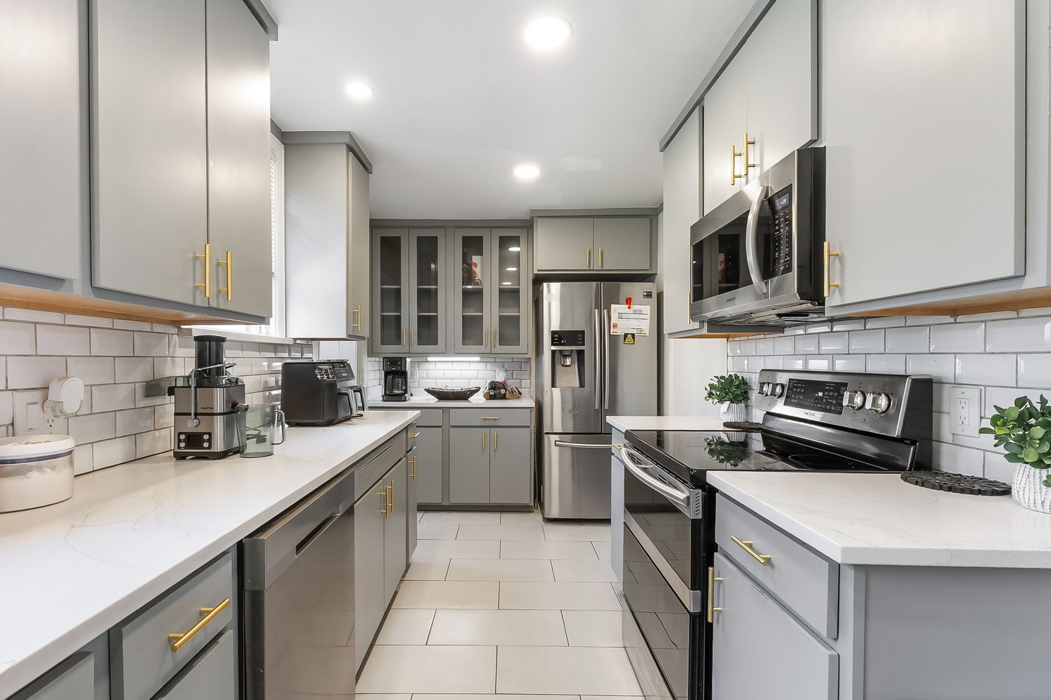 Modern kitchen with gray cabinets, gold hardware, white quartz countertops, subway tile backsplash, and stainless steel appliances.