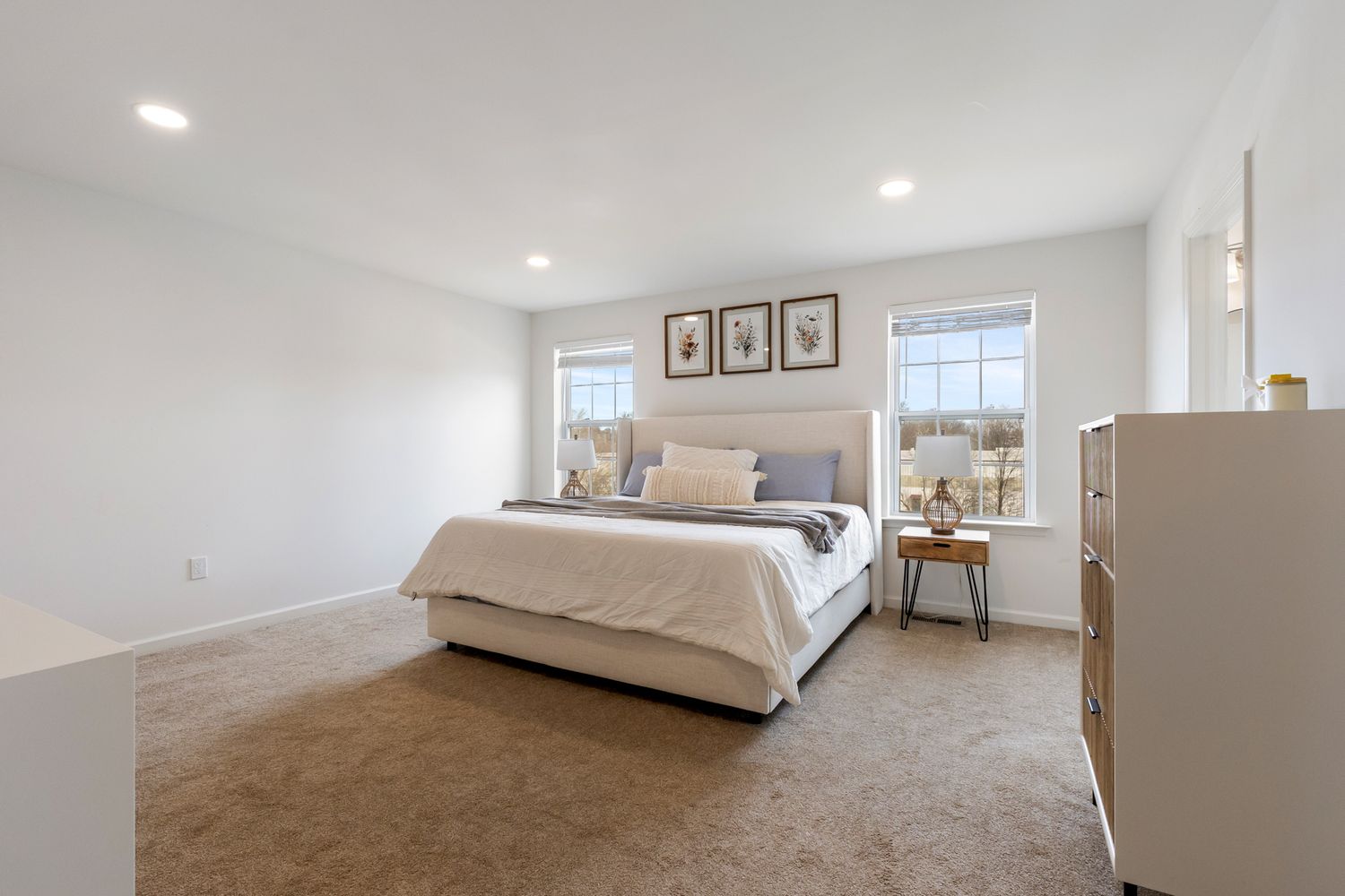Spacious master bedroom with neutral carpet, large windows, and a king-sized bed in a modern home.