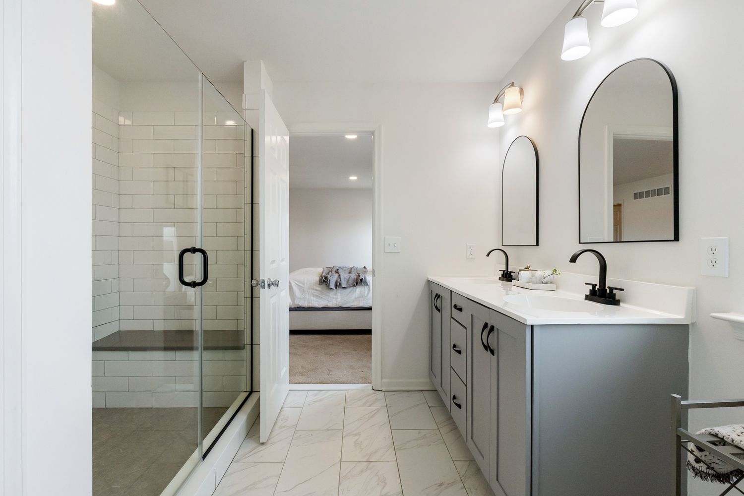 Modern white bathroom interior with subway tile walls, floating vanity, and arched mirror features clean lines and bright lighting.