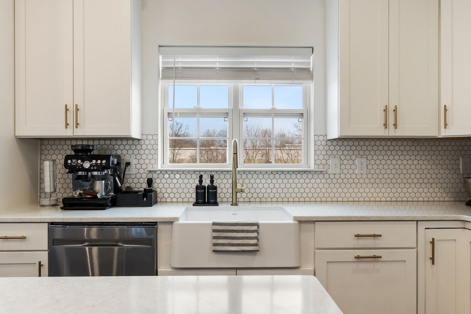 Modern white kitchen with hexagonal backsplash tiles, quartz countertops, and gold hardware accents.