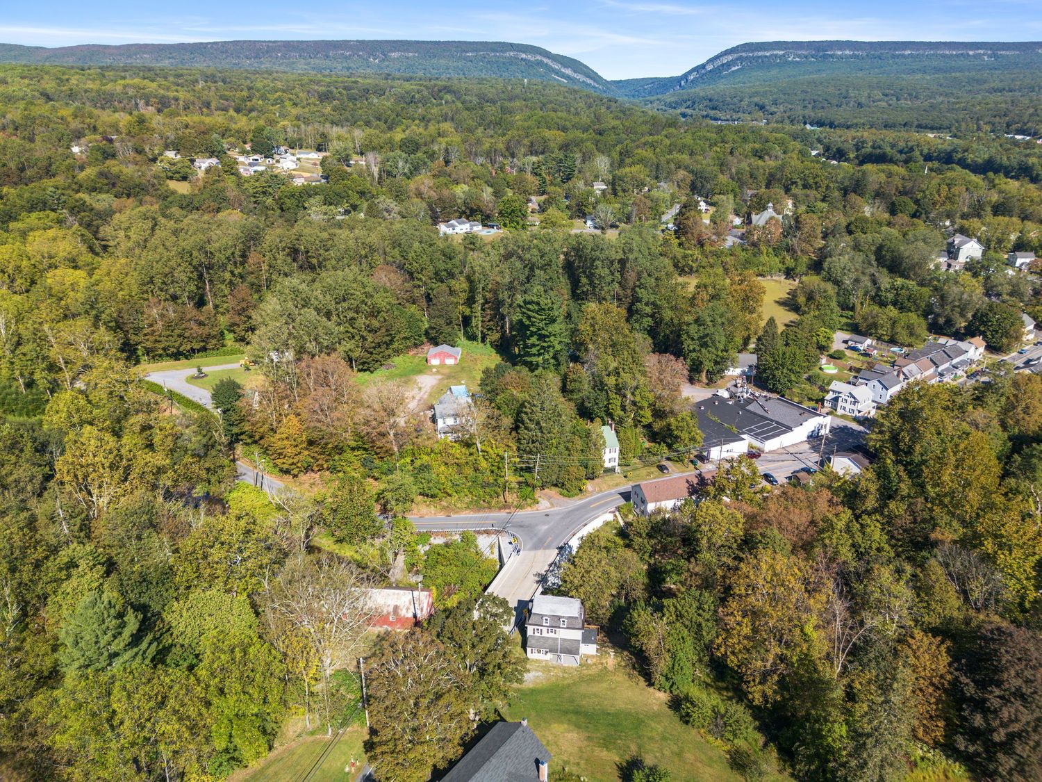 Panoramic drone shot of homes and buildings situated along rolling hills and wooded areas.