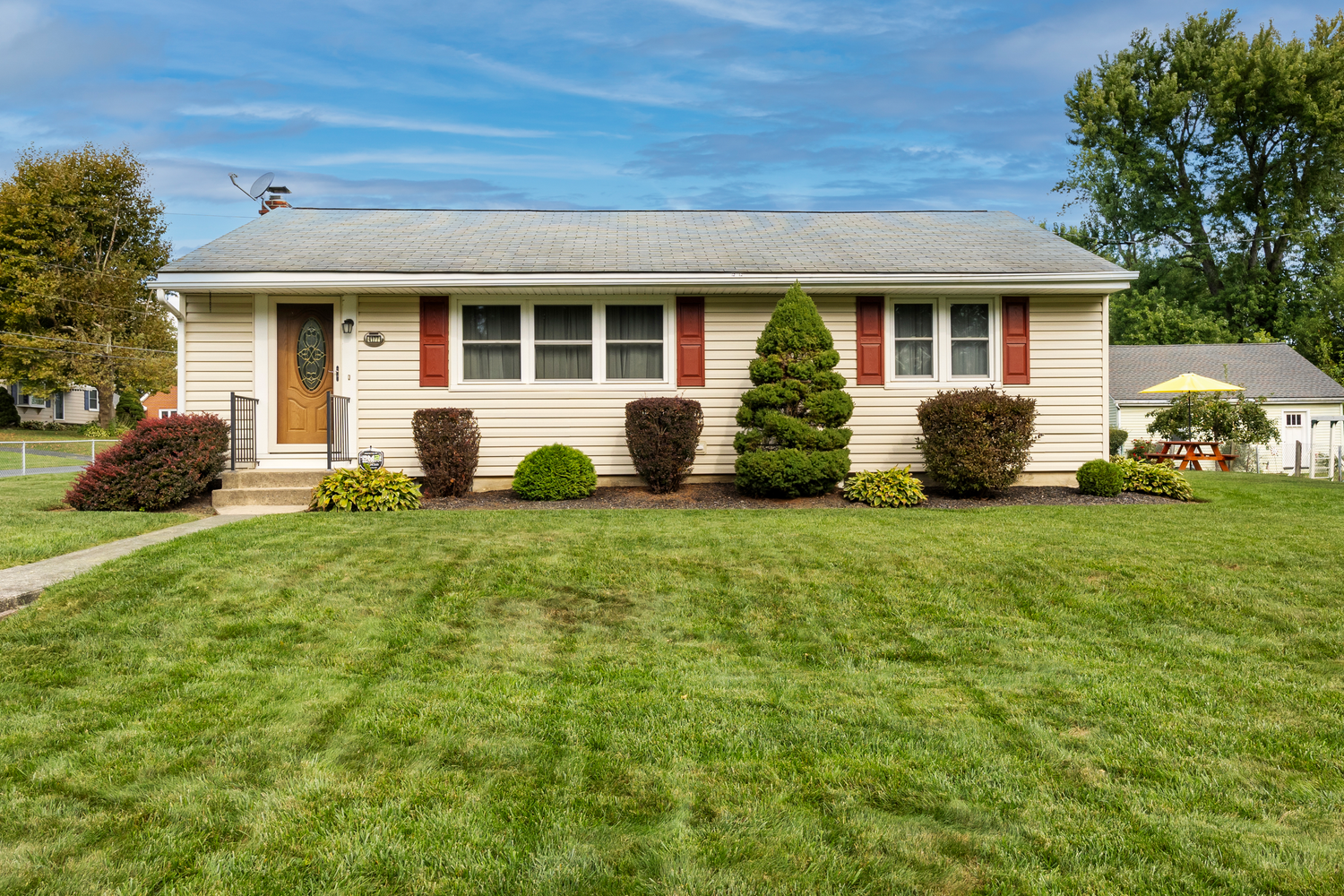 Well-maintained ranch style home with green lawn and landscaping under blue sky.