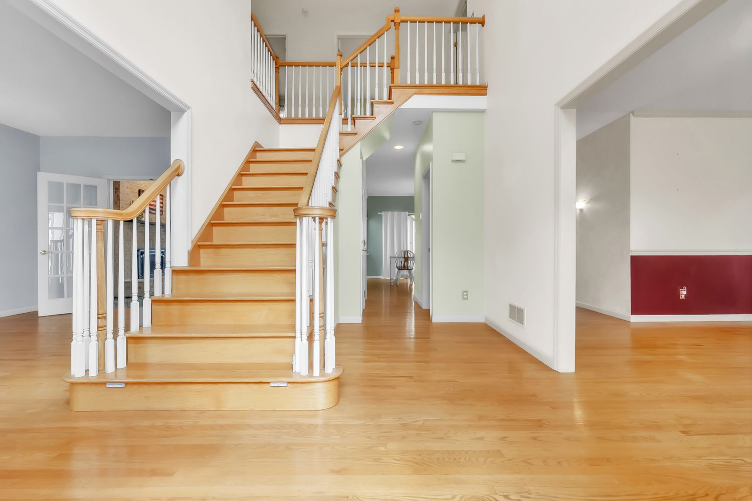 Bright open-concept living area with hardwood floors, white walls, and an elegant wooden staircase leading to the second floor.