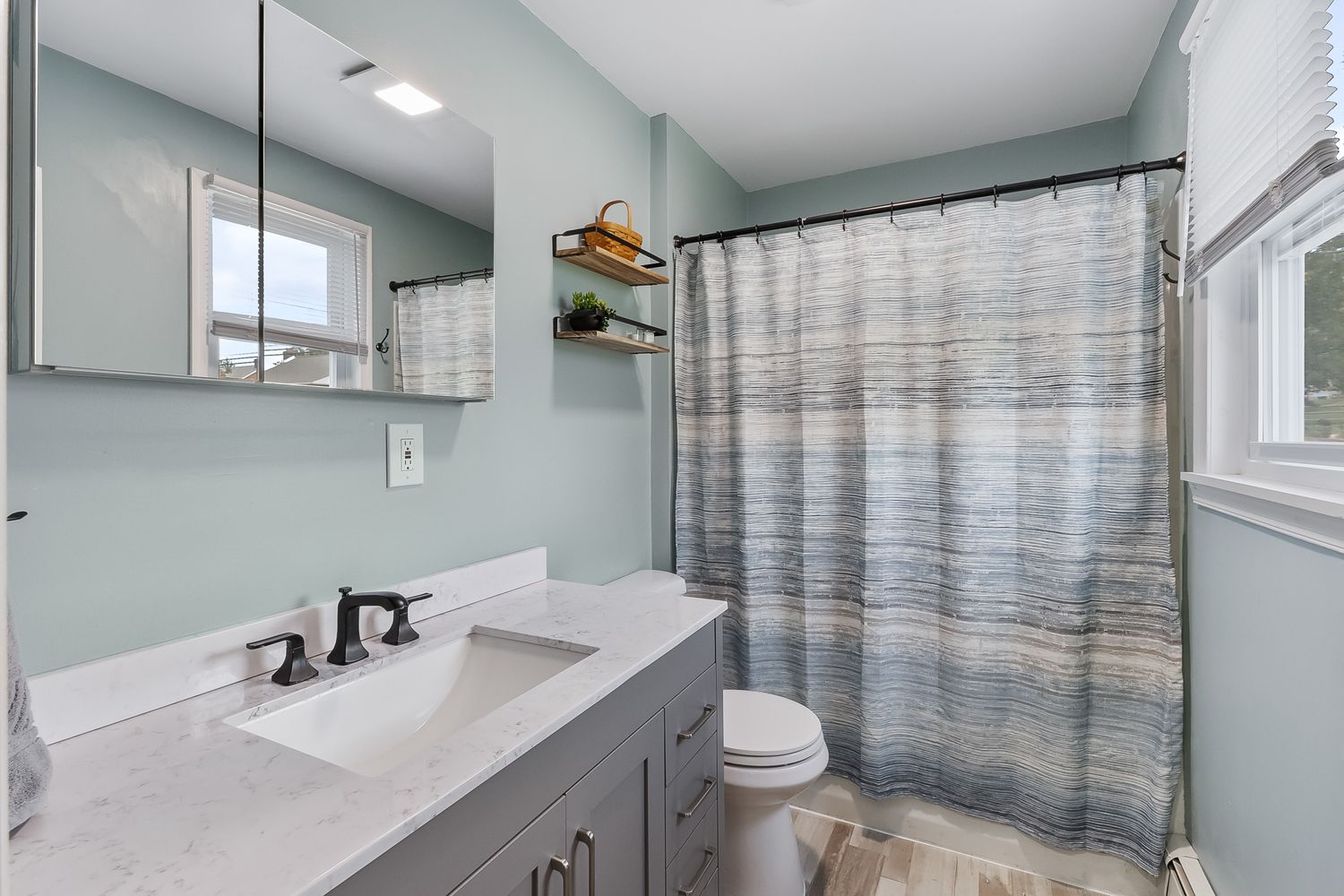 Modern bathroom with gray tile, glass shower enclosure, and seafoam green walls.