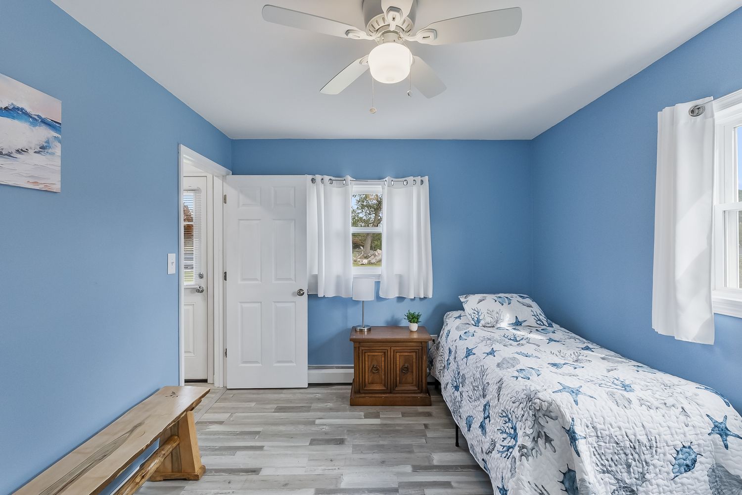 Bright bedroom with blue walls, white trim, and ceiling fan featuring coastal decor.