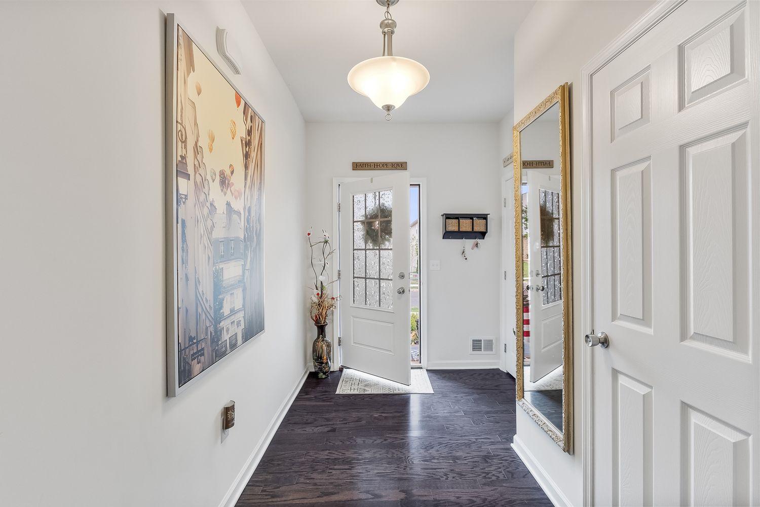 Long bright white hallway with hardwood flooring and multiple doorways.