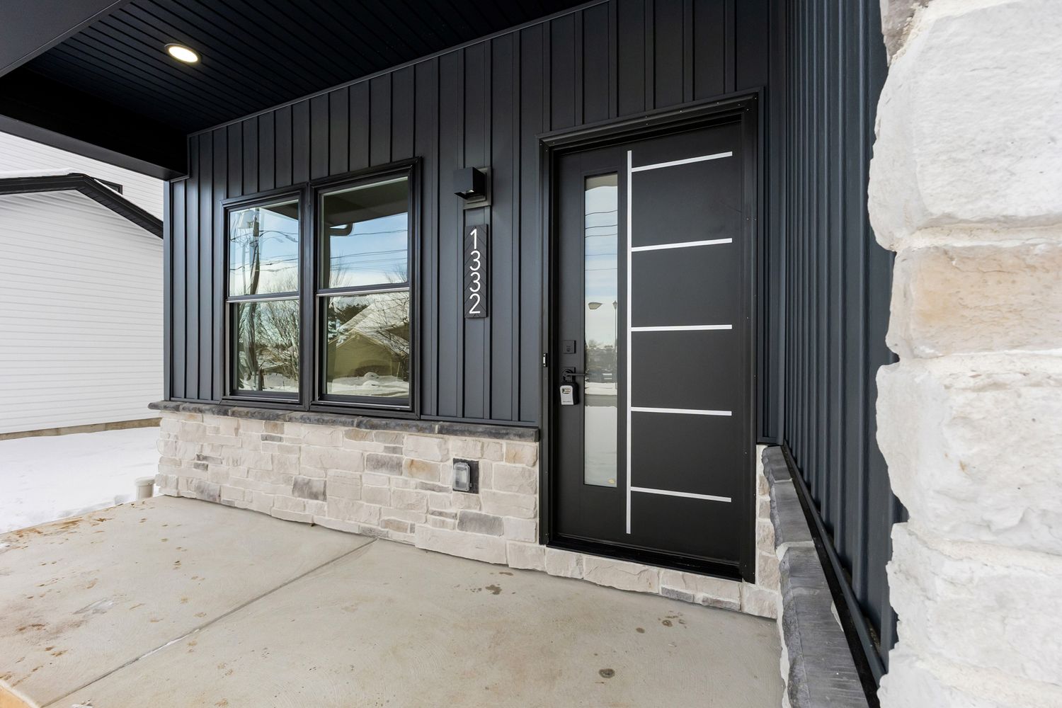 Modern black front door with glass panels and sleek hardware mounted on dark gray exterior siding.