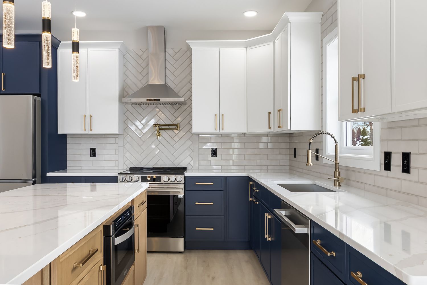Modern kitchen design features white cabinets, navy blue accents, gold hardware, and chevron tile backsplash.