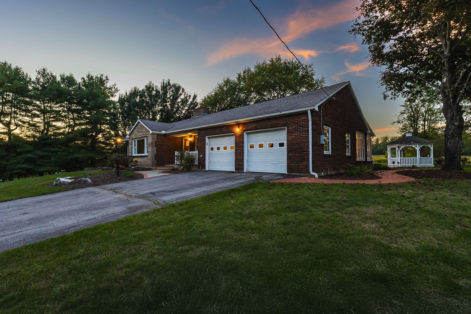 Wide-angle view of residential property with paved driveway and landscaped yard at dusk.
