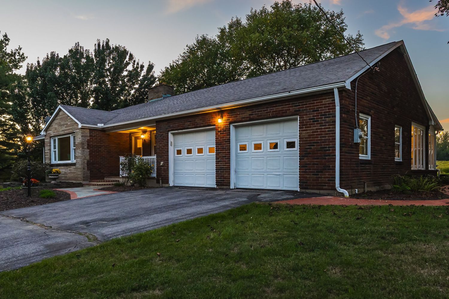 Exterior view of brick ranch home with attached garage at sunset.