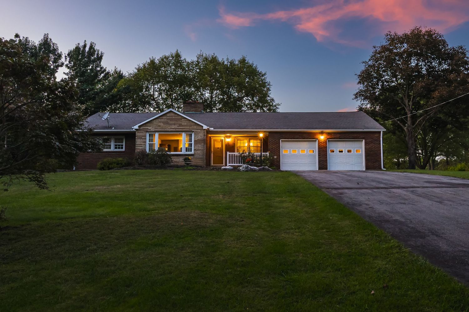 Modern ranch house with two-car garage and manicured lawn photographed at sunset.