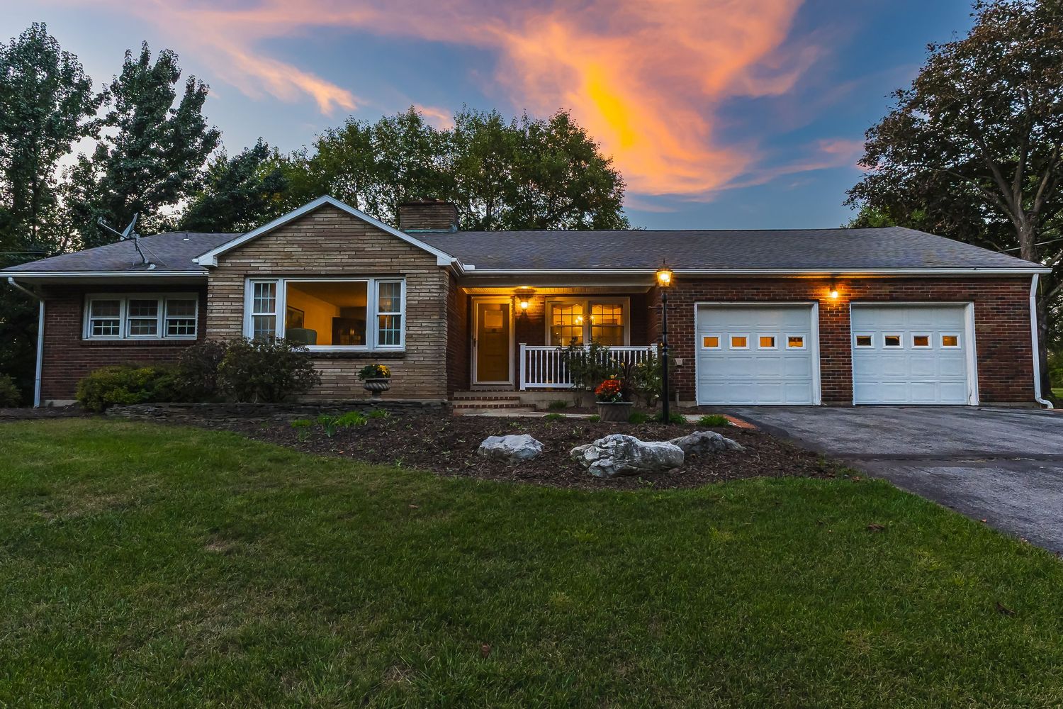 Panoramic view of a ranch house with attached garage at sunset with warm orange sky and glowing windows.