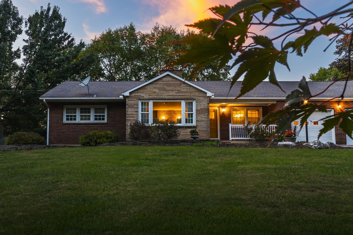 Panoramic view of single-story brick home with landscaping at golden hour.