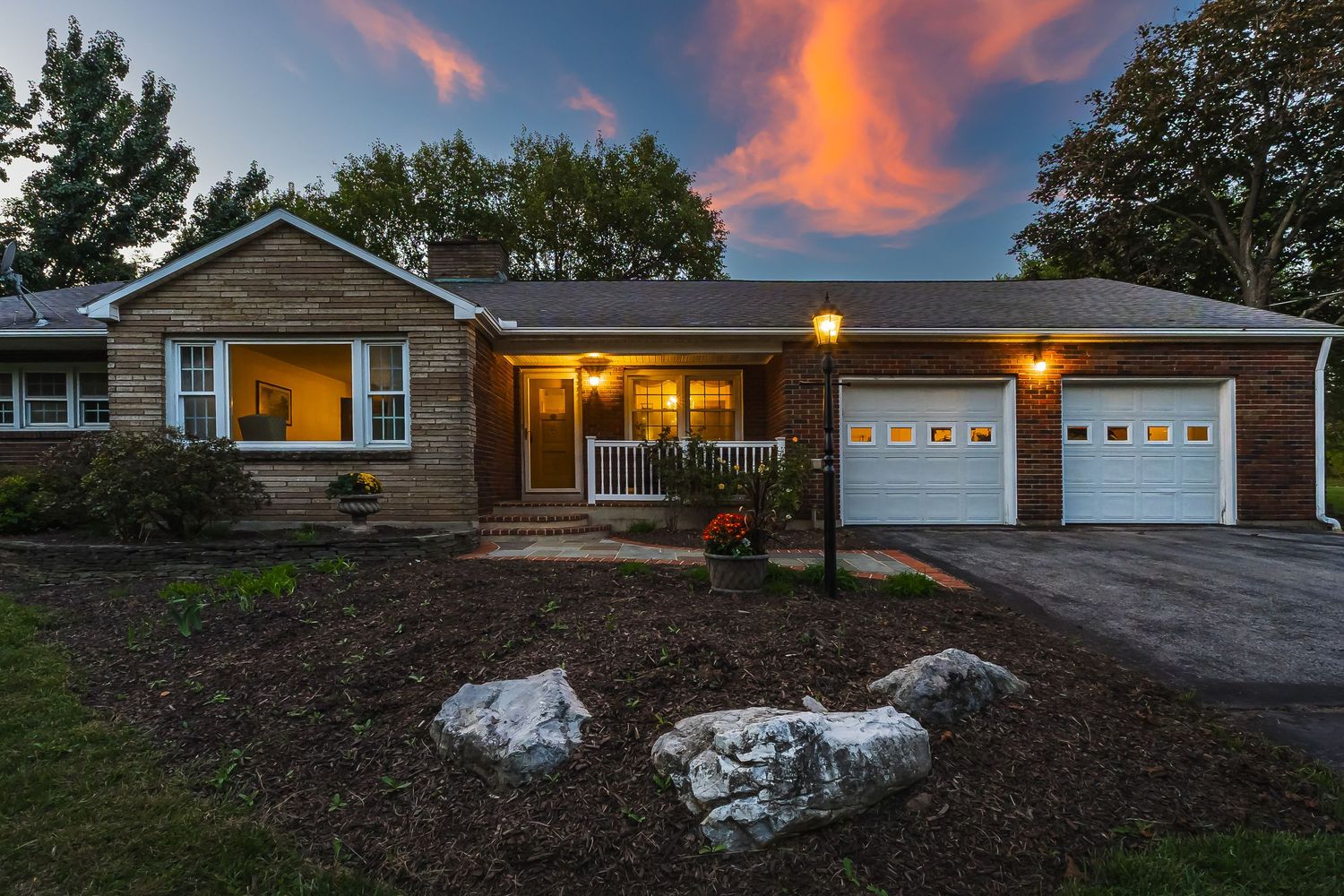 Dramatic sunset view of residential home with attached garage and sloping lawn.