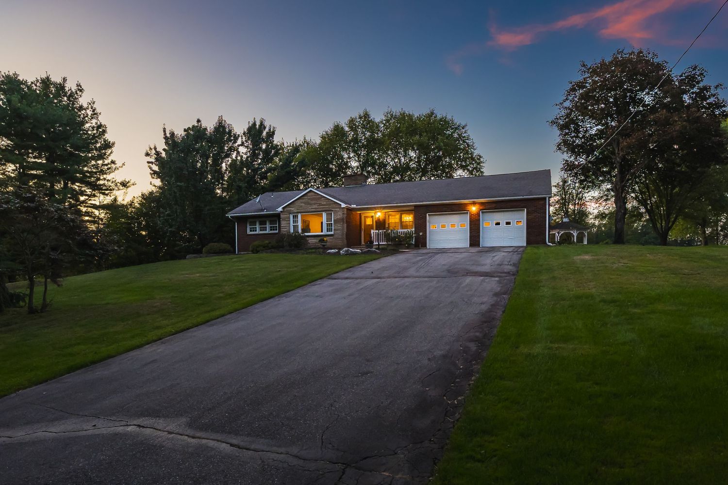 Scenic view of a suburban home with long driveway against a twilight sky with pink clouds.