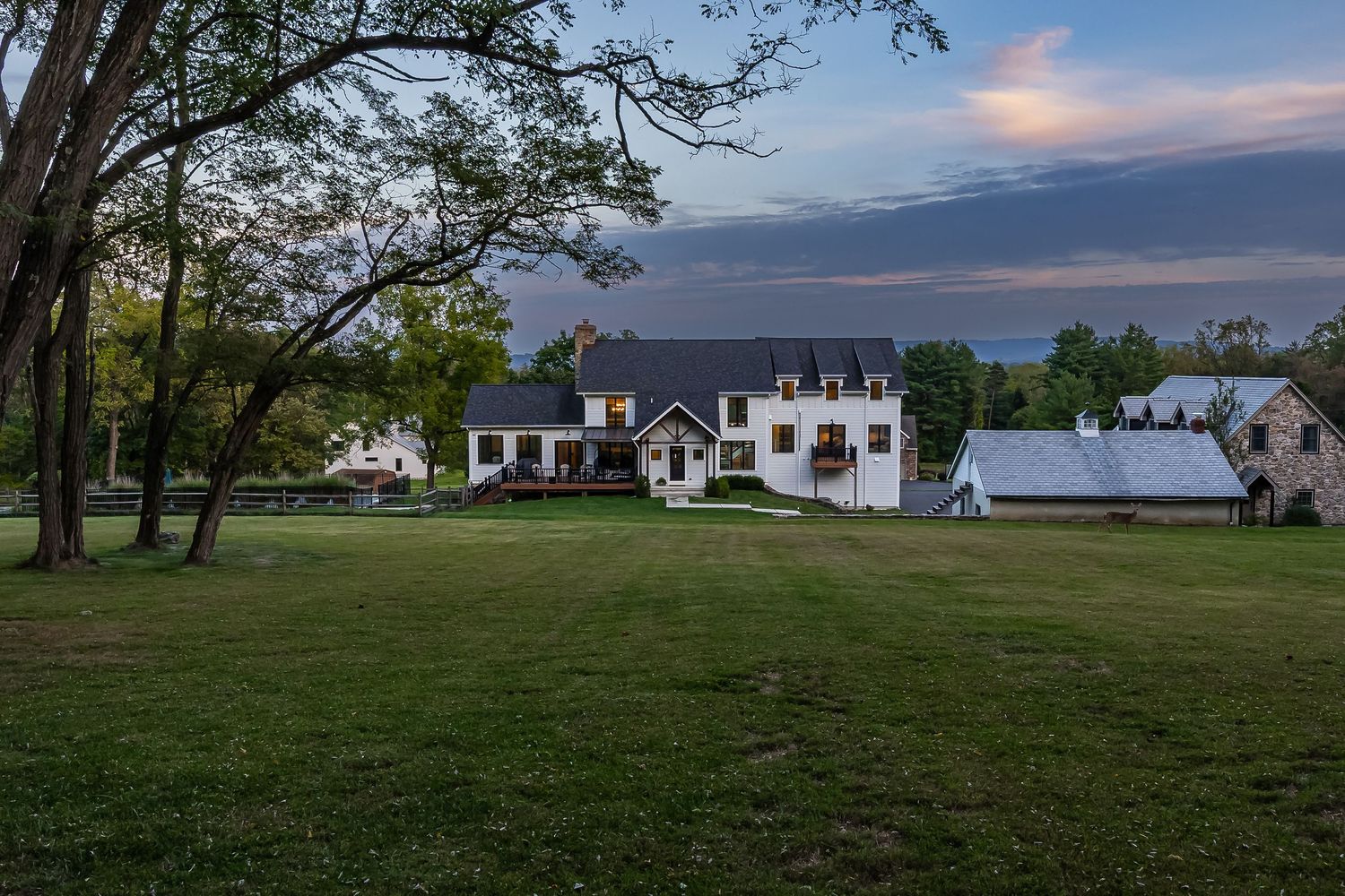 White farmhouse-style homes nestled among trees at dusk with rolling hills in the background.