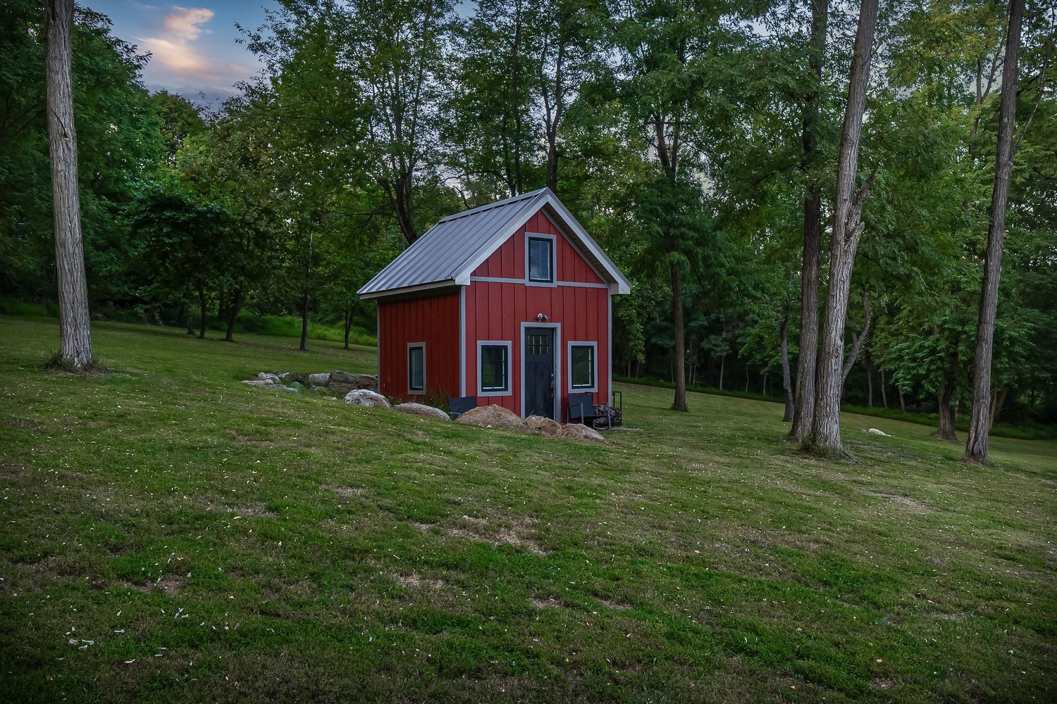 Red barn-style outbuilding nestled on a hillside among tall trees and natural landscaping.