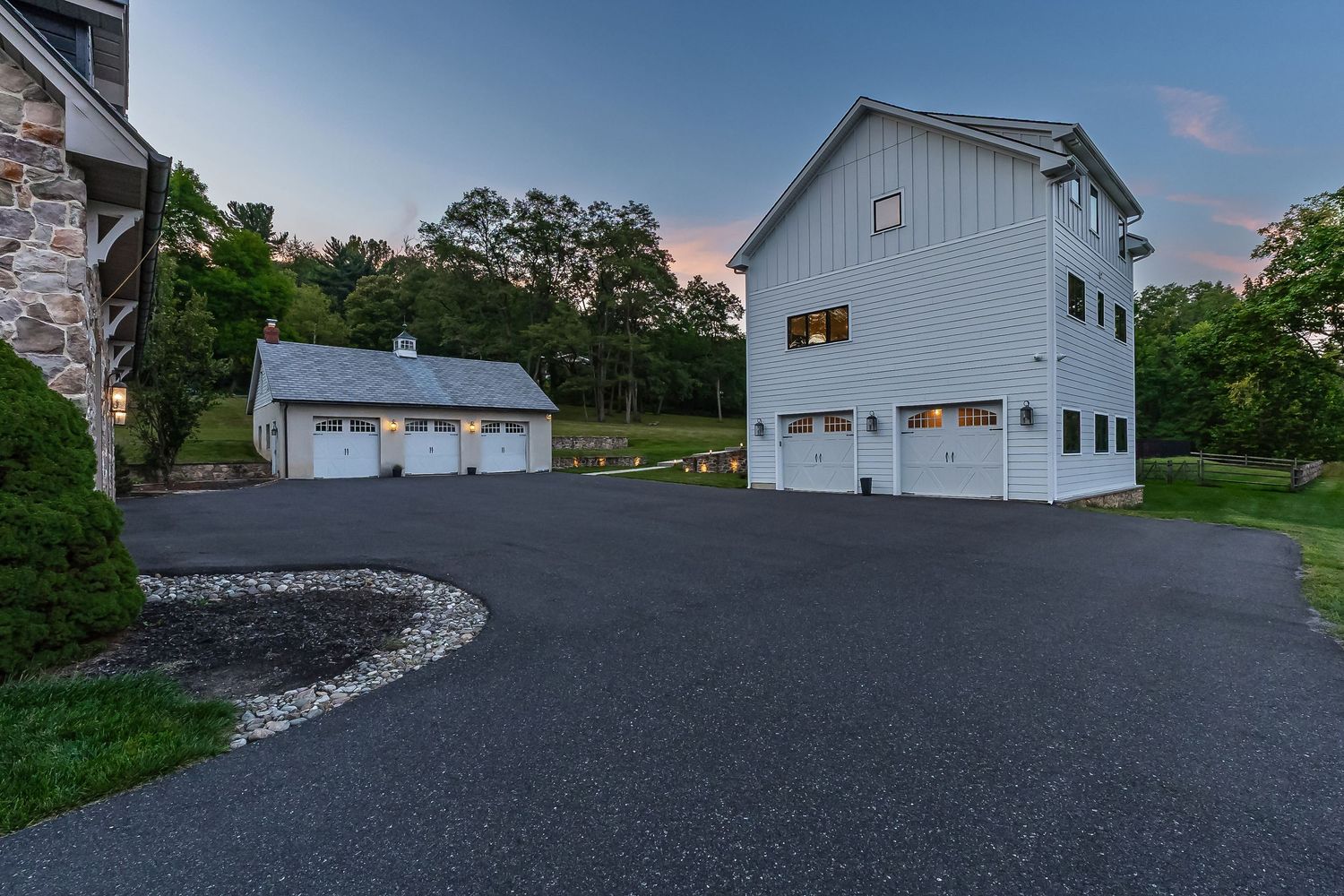 White detached garage buildings with multiple doors on paved driveway at twilight.
