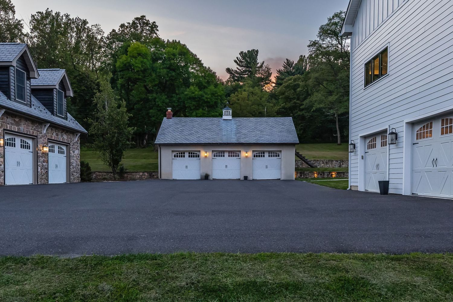 Three white garage buildings with multiple doors arranged around a paved courtyard at sunset.