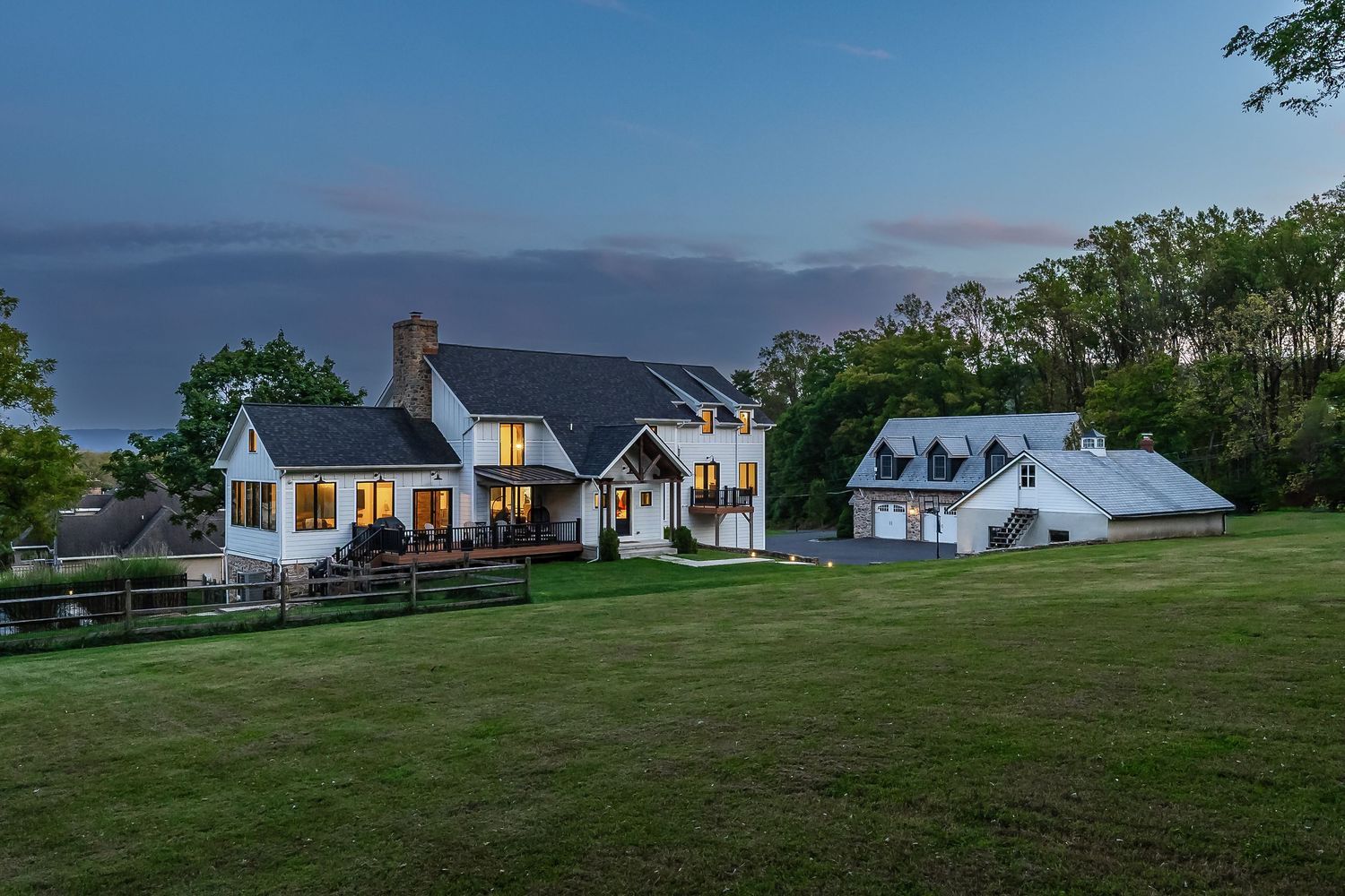 Stunning modern farmhouse estate with detached garage buildings glowing at twilight.