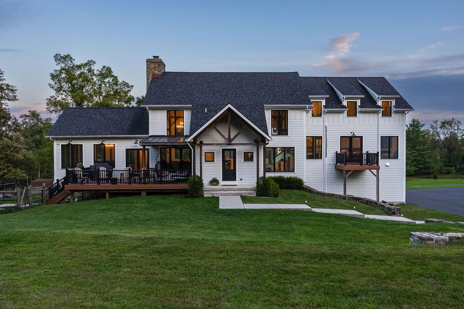 Modern farmhouse style home with white exterior and dark roof illuminated at dusk on a spacious lawn.