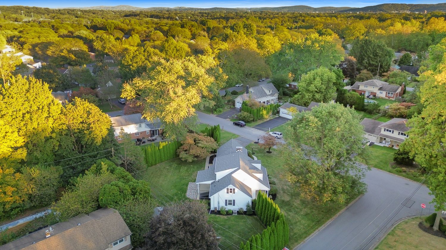 Aerial view of a suburban neighborhood with autumn foliage and winding roads at sunset.