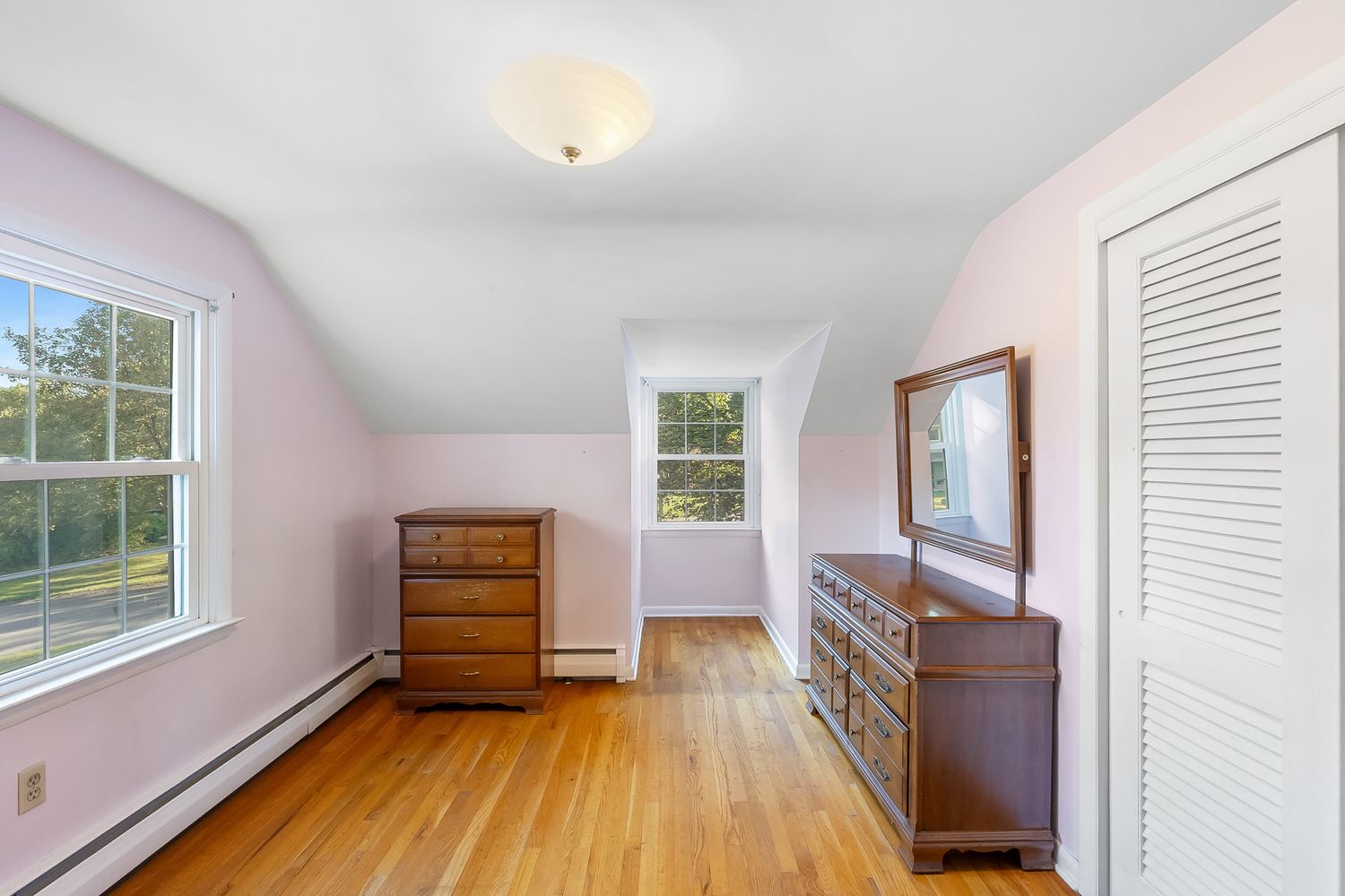 Long attic bedroom with sloped ceilings, hardwood floors, and natural light from multiple windows.