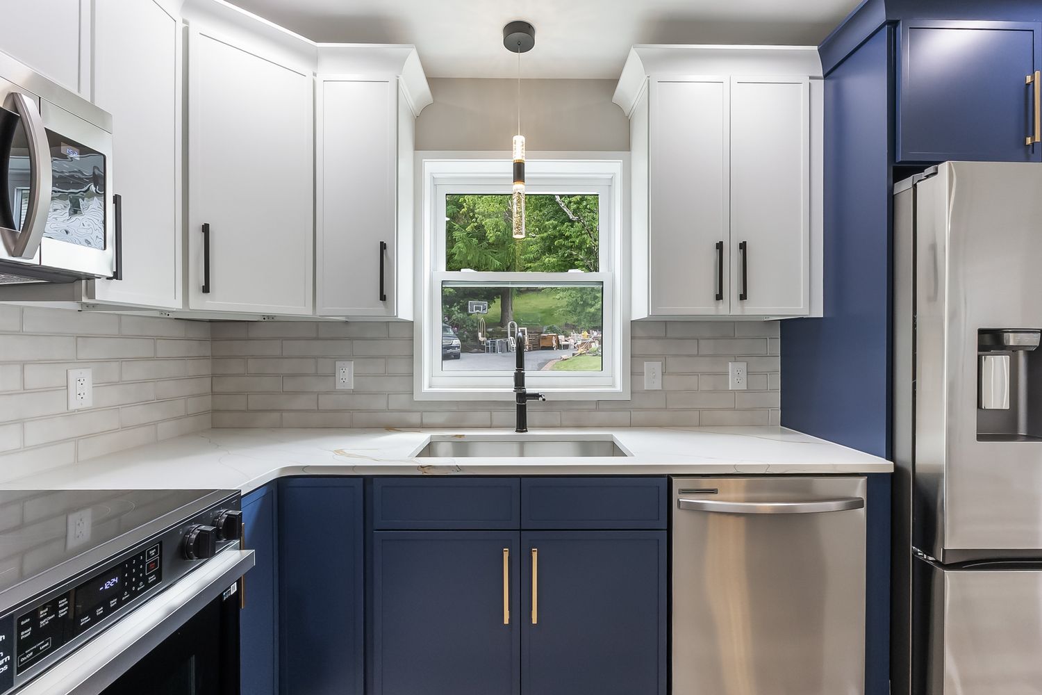 Modern kitchen with navy blue lower cabinets, white upper cabinets, subway tile backsplash, and stainless steel appliances.
