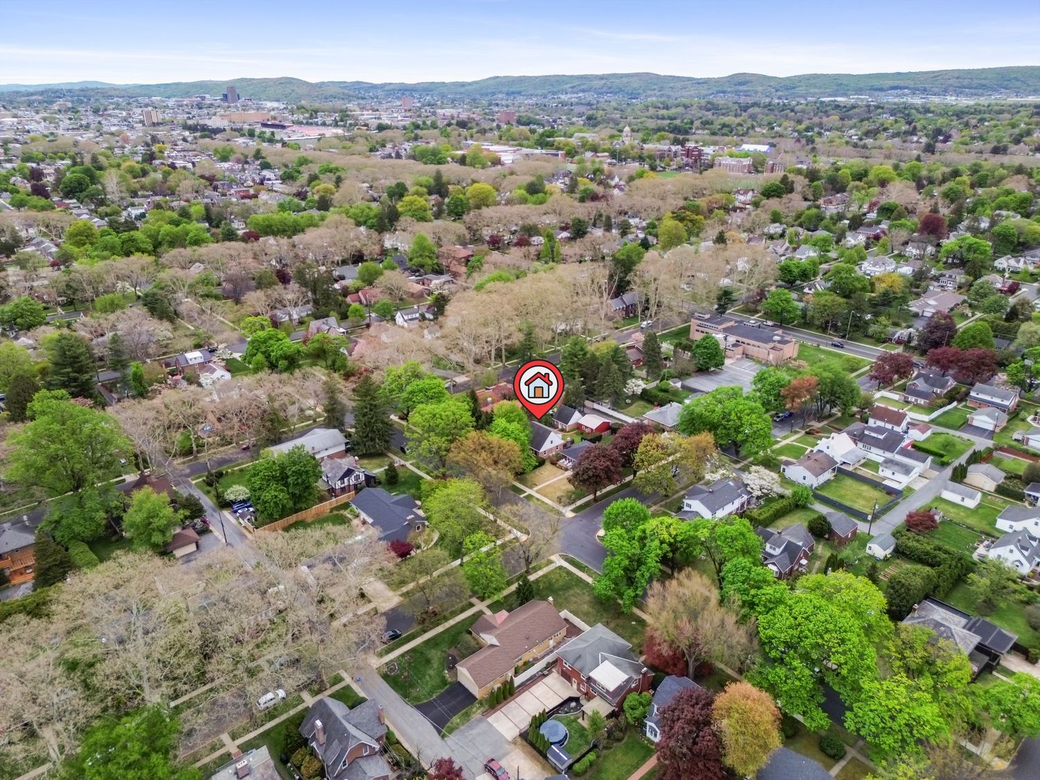 Aerial drone view of a suburban neighborhood surrounded by lush green trees with a marked property in the center.