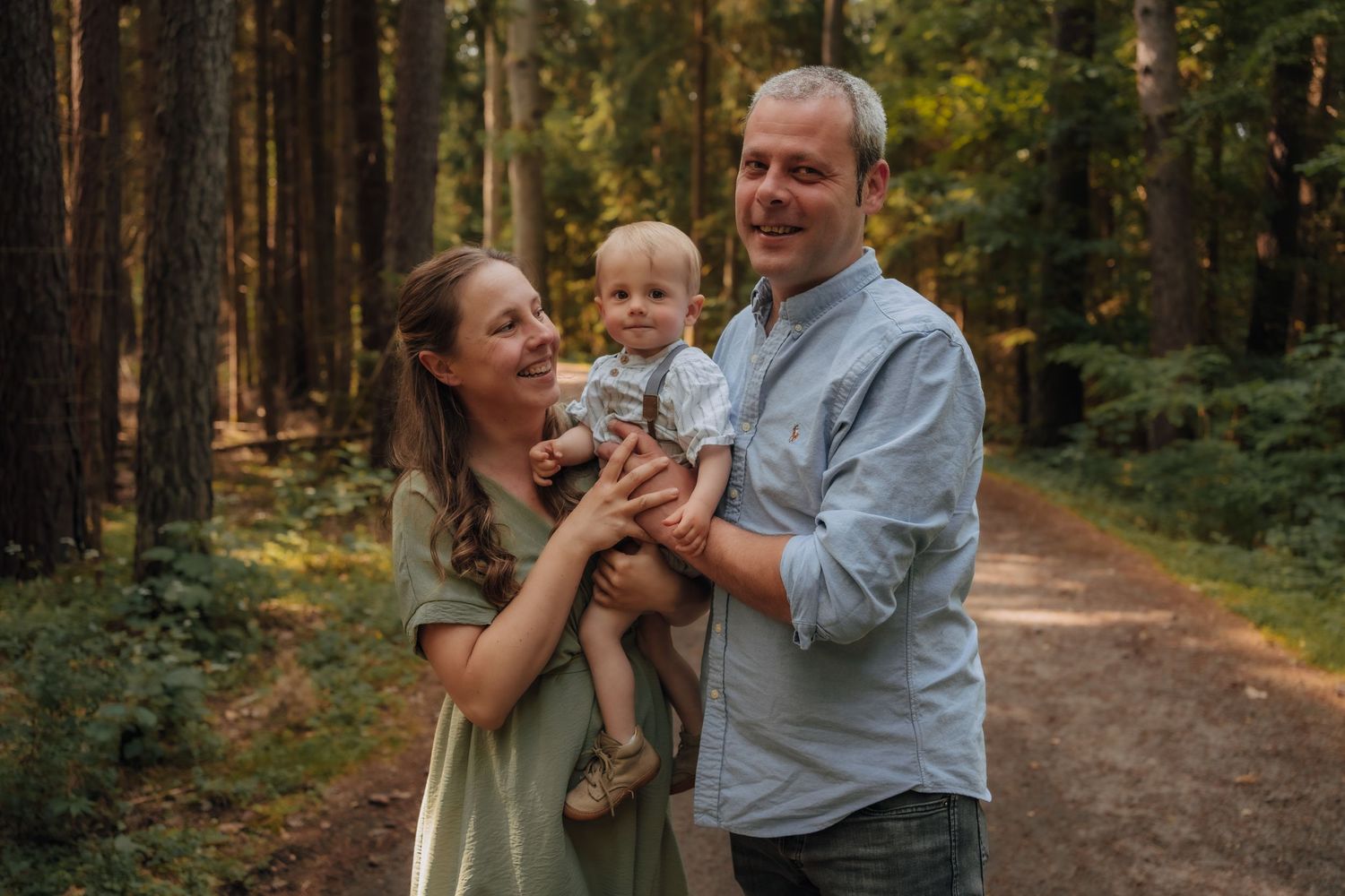 A family shares a joyful moment together while standing on a forest path surrounded by tall pine trees.
