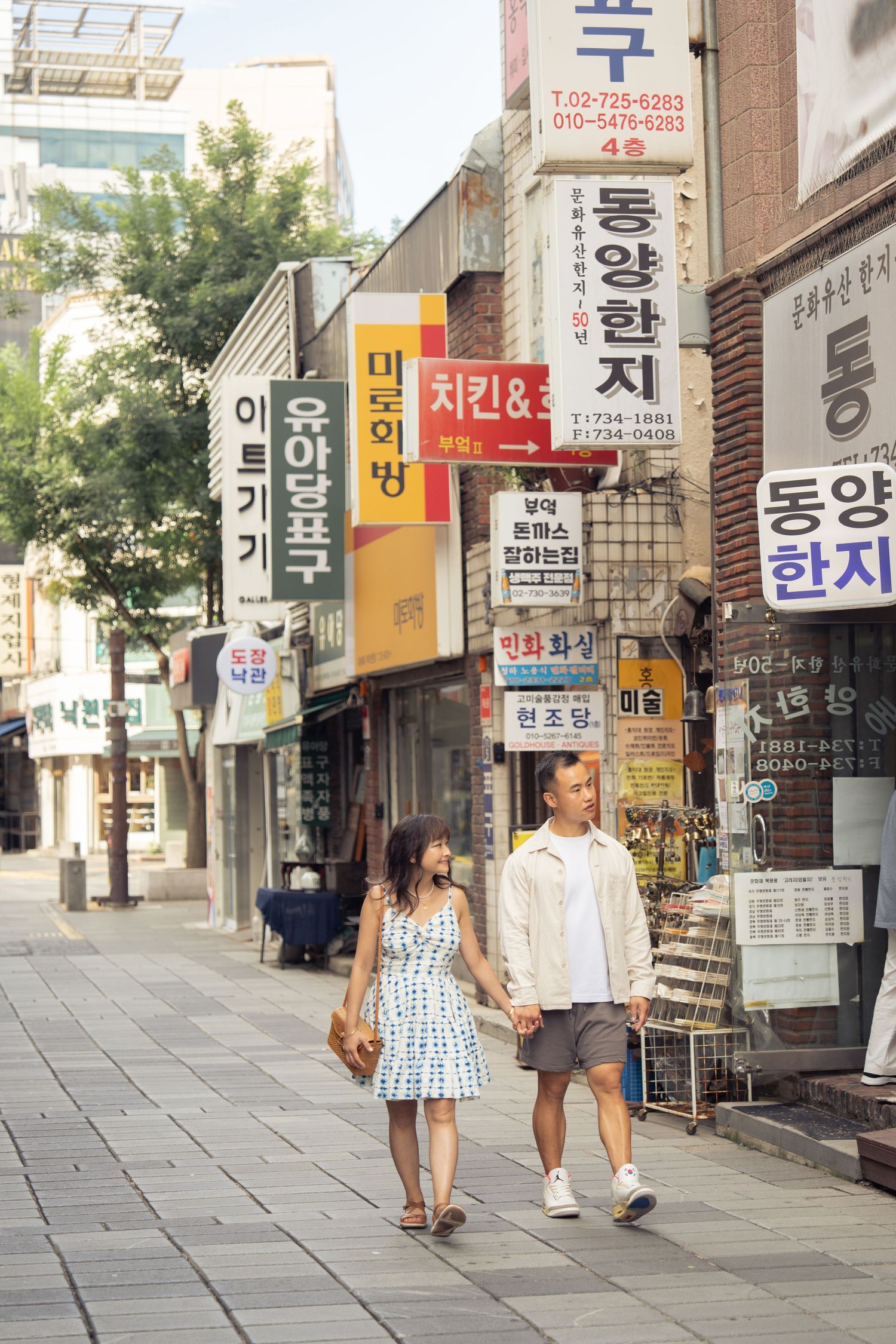 People walking down a street with Korean signage and storefronts on a sunny day.
