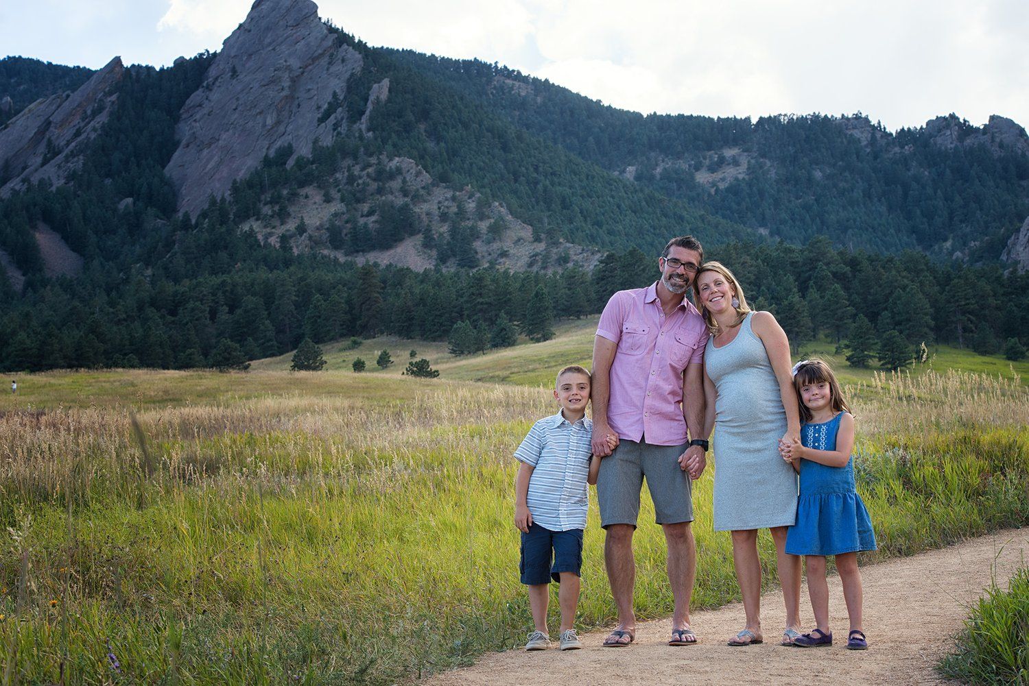 A Erie Colorado couple stands together on a hiking trail with scenic mountain views and wildflower meadows in the background.
