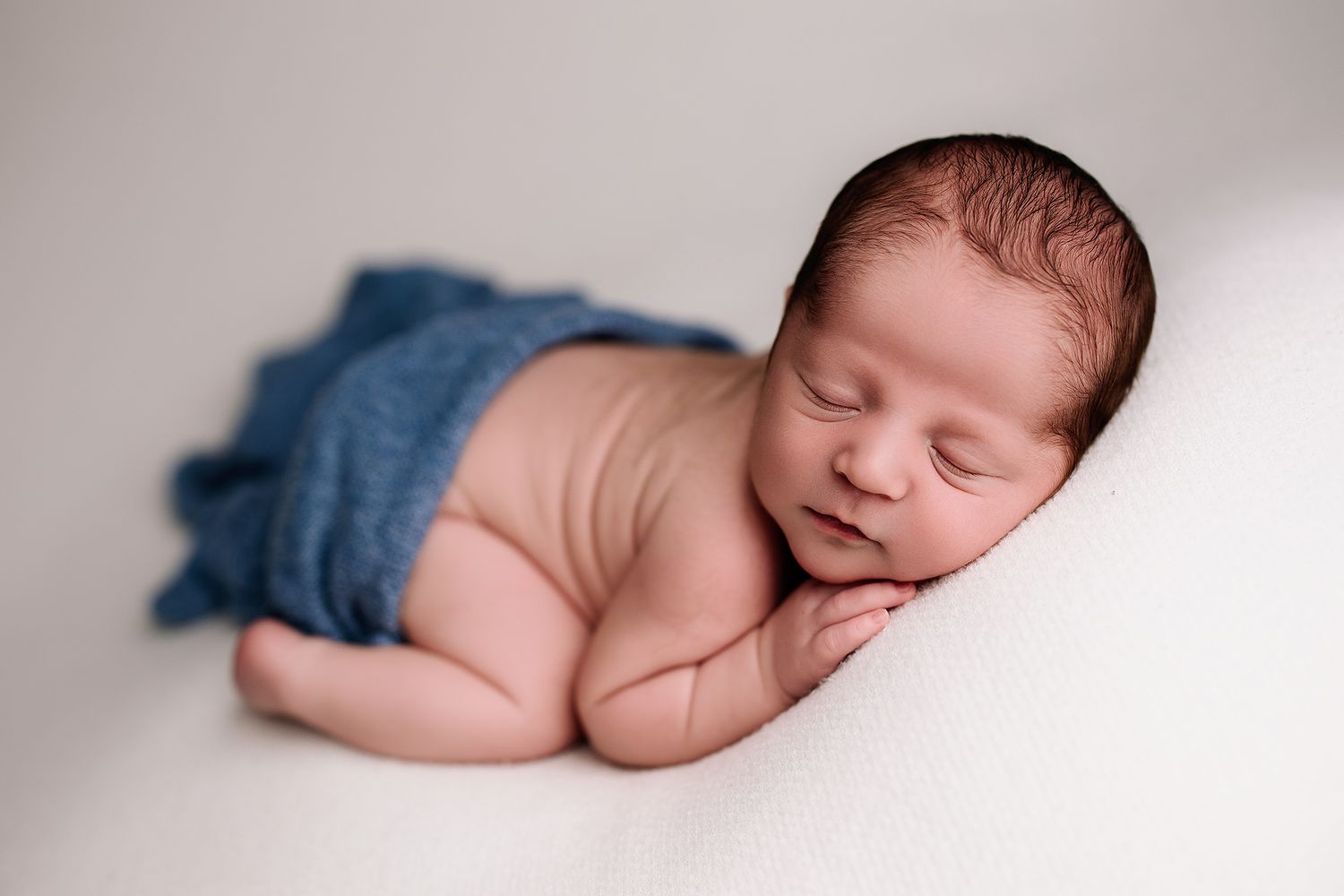 5 star review of newborn photographer in the Kansas City area. highly rated by customers. Baby boy posed and sleeping on white blanket