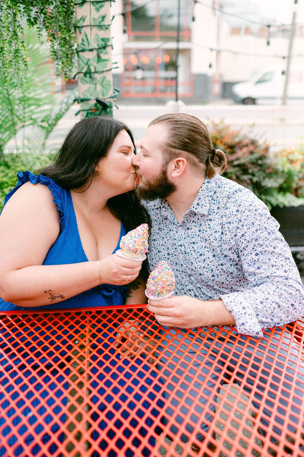 A couple sharing an intimate moment while sitting at a red metal table outdoors.