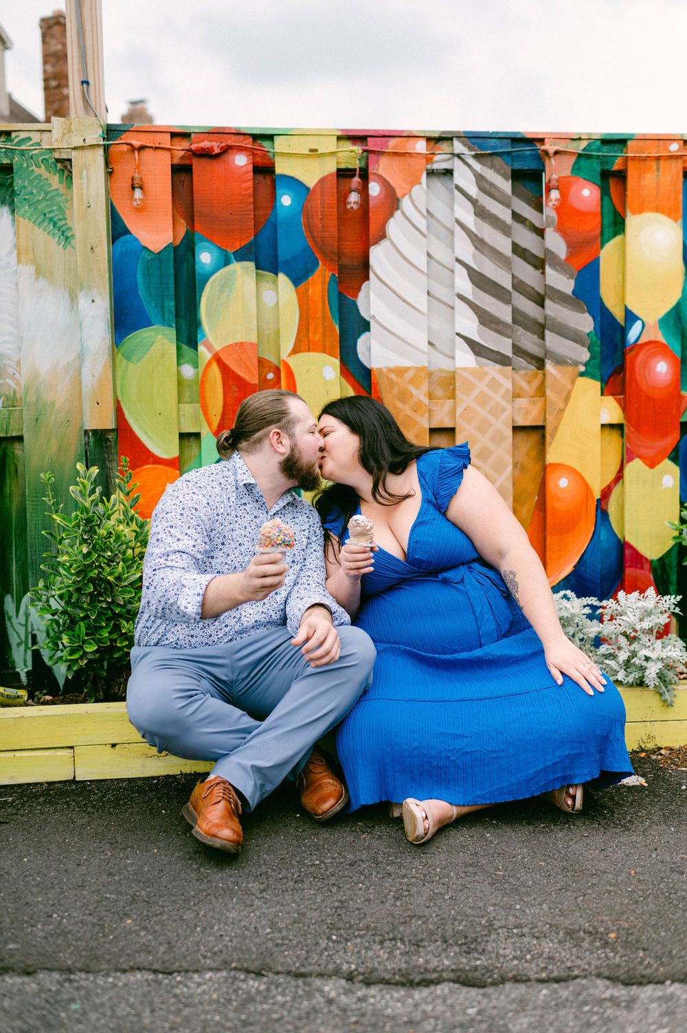 A couple sitting together against a colorful geometric mural wall sharing a tender moment.