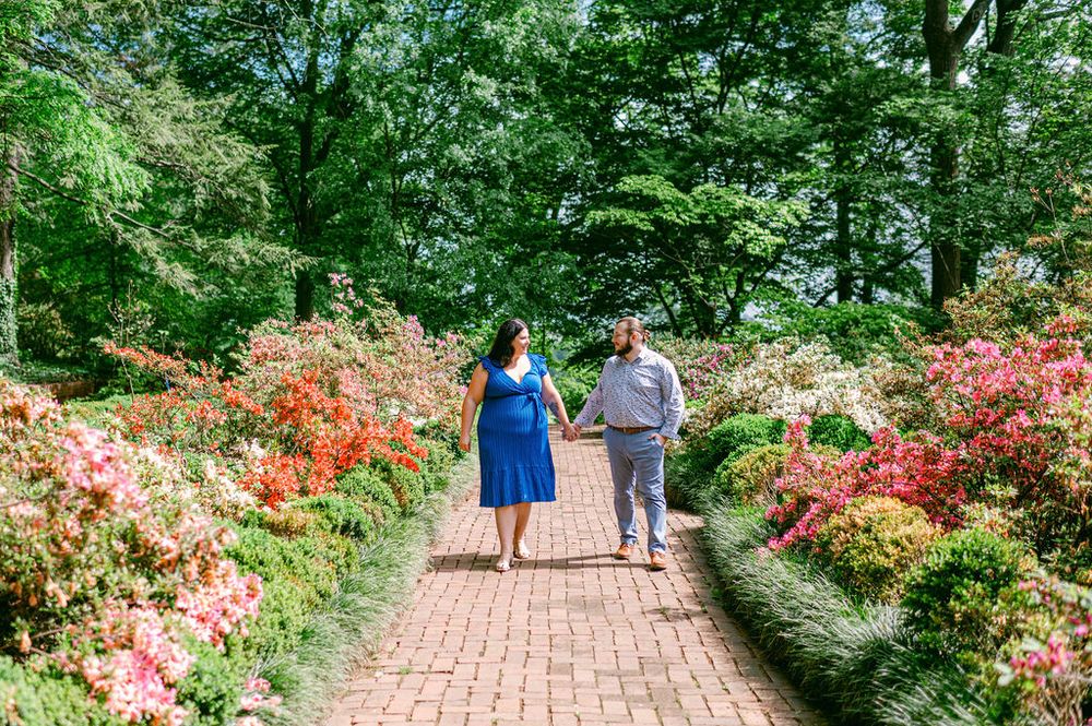 A brick pathway winds through a vibrant garden filled with blooming azaleas and lush greenery.