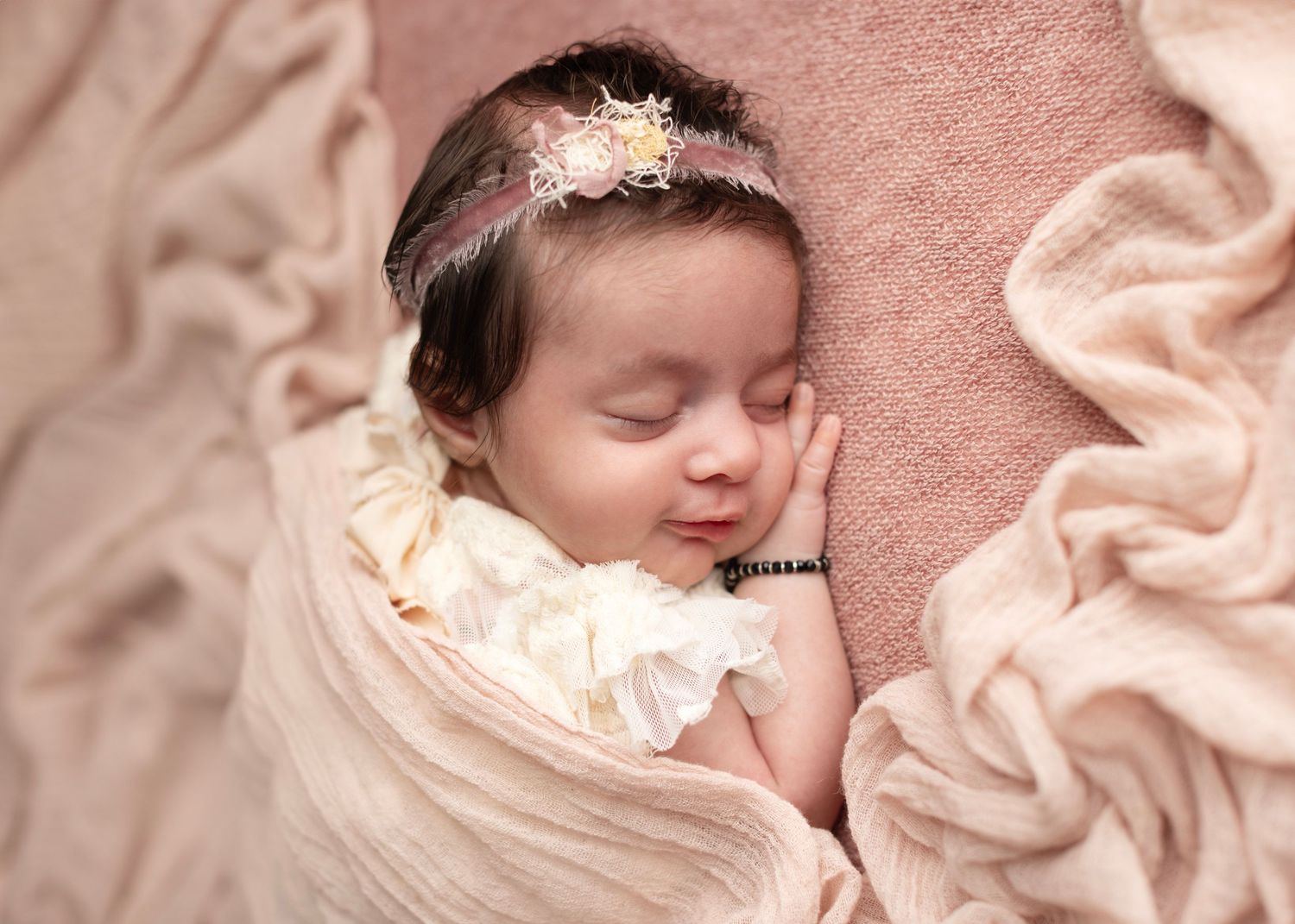 A sleeping baby rests peacefully on soft pink blankets with a delicate white lace collar.
