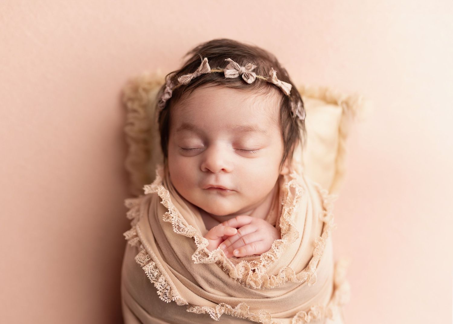 A sleeping newborn baby wrapped in soft beige lace fabric during a professional photography session.