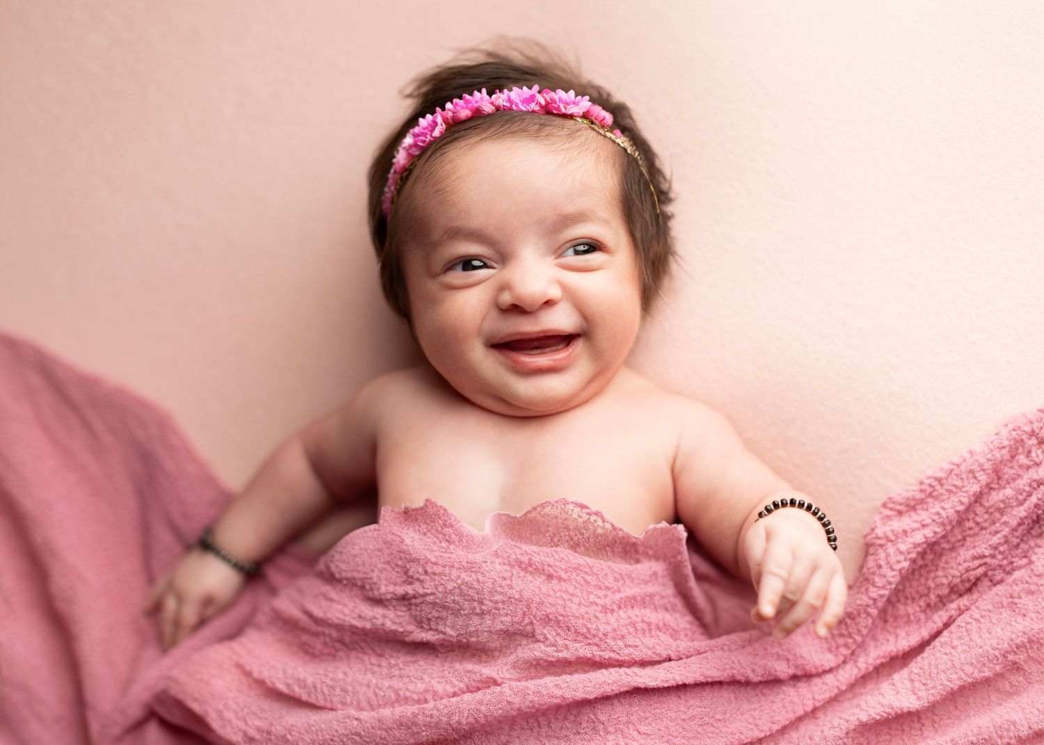 Baby wrapped in soft pink blanket smiling while laying on plush surface.