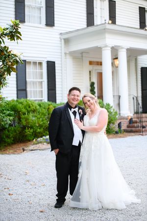 A couple shares a romantic moment in front of a white colonial style house with black shutters on their wedding day at primrose cottage